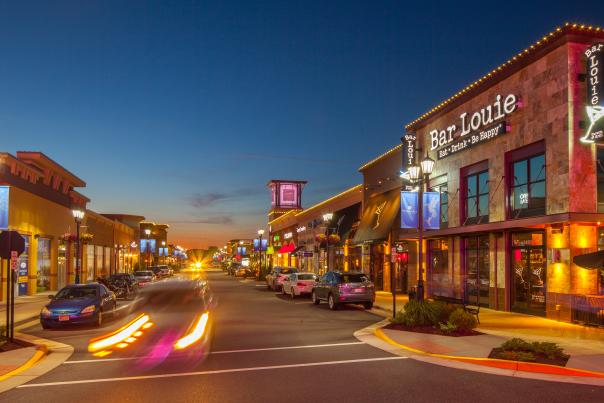 A shopping area at night with cars going by