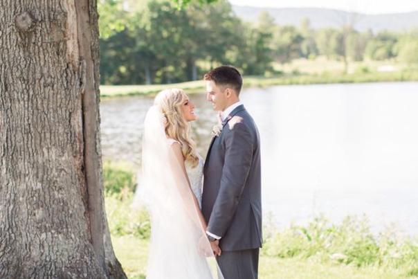bridge and groom standing beside tree in front of water