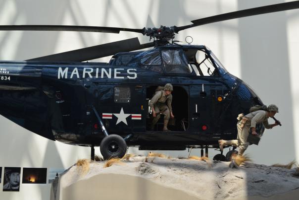 a navy helicopter with the word "marines" on the front with 2 statues of men coming out of the helicopter