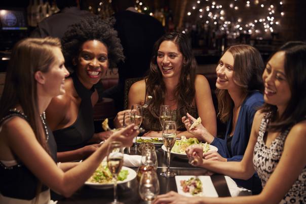 A group of women at a restaurant with wine and food in front of them.