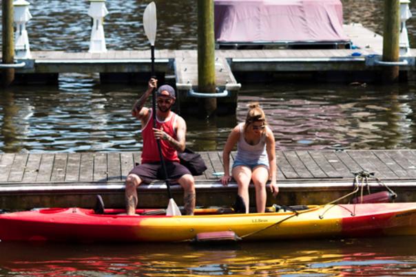 A man and a woman sitting on a boardwalk getting ready to get into a kayak
