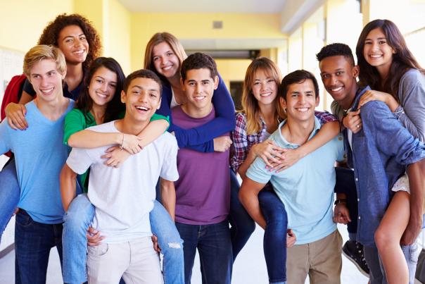 A group of smiling high school age kids in a hallway