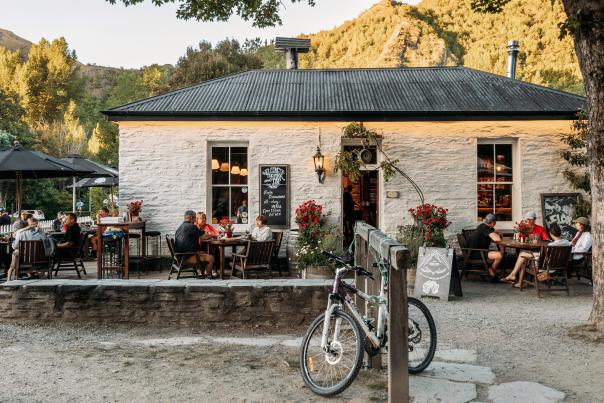 Old white cottage-looking pub with people sitting al fresco and green mountains in the background