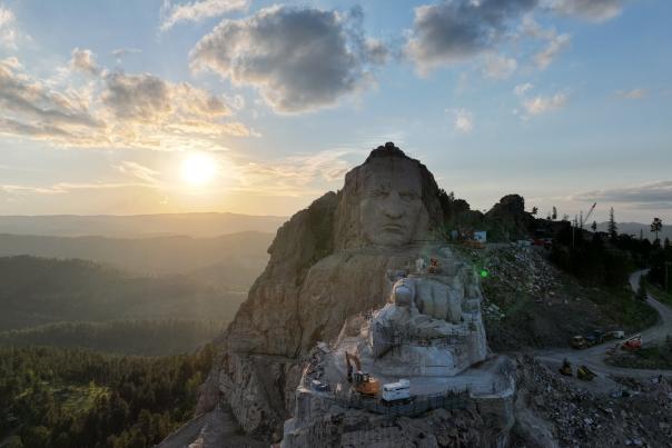looking straight on at Crazy Horse memorial with the sun setting and black hills behind the statue