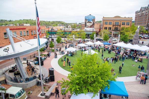 A high vantage point photo of Main Street Square while a band plays on the stage and shoppers browse the vendors in tents on the grass.