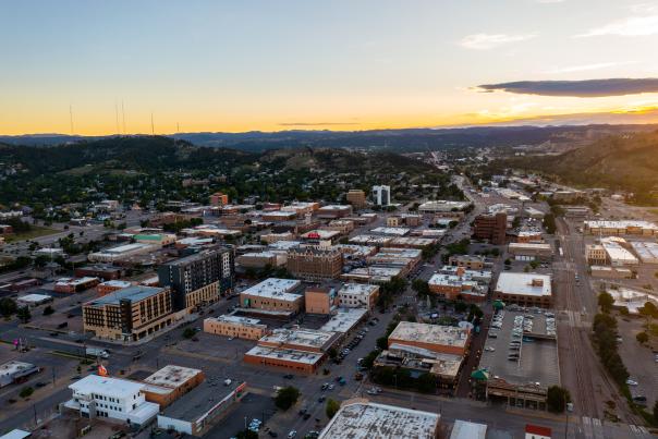 Aerial view of downtown Rapid City at sunset with the Black Hills stretching across the horizon.