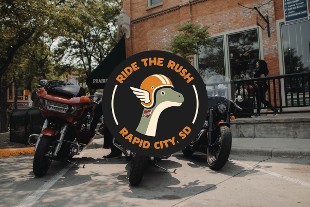 A logo of Ride The Rush is superimposed over a photo of three motorcycles parked along the curb in Downtown Rapid City.