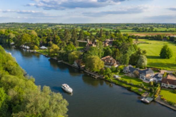 a boat cruising along the river thames surrounded by countryside.