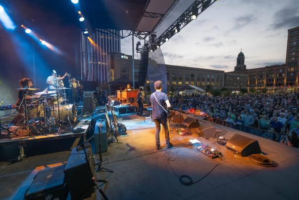 Musician on stage performing to a crowd while playing a guitar during the Rochester International Jazz Festival