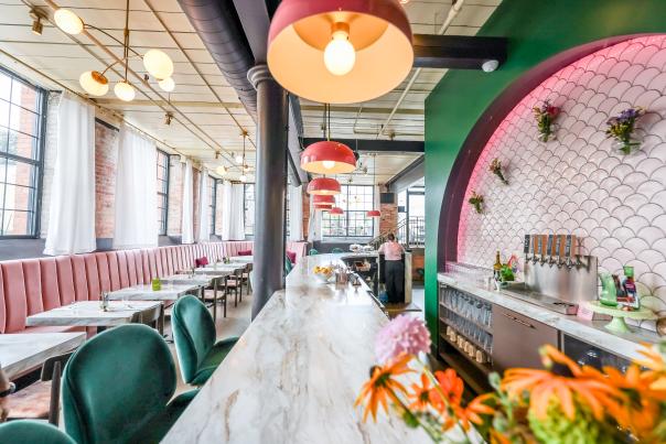 Interior of Petit Poutinerie with pink lampshades, marble bar, green velvet chairs and a pink booth