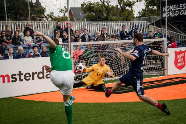 A soccer player taking a shot at a goal, and a keeper stretching to block the shot