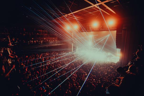 Crowd-filled concert at Channel 24 in Midtown Sacramento, with bright stage lights and blue laser beams illuminating the audience.