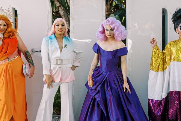 drag queens dressed in colorful clothing standing in front of letters that spell PRIDE