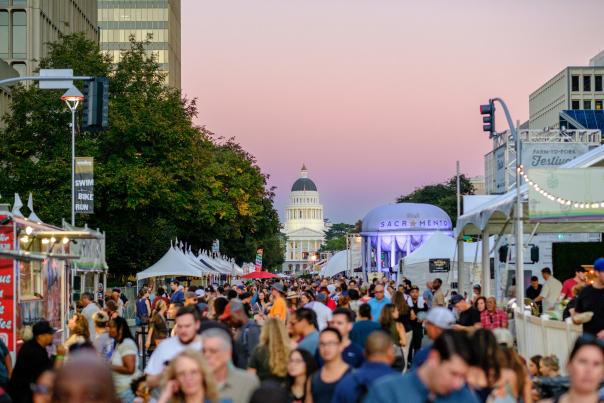 a crowd walking around a festival at night with the capitol building in the background