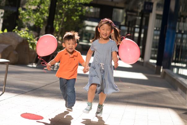 Two happy kids running in an urban environment. They have red balloons