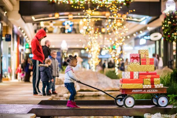 A child pulling a radio flyer wagon full of presents with shoppers in the background