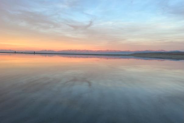 Great Salt Lake at sunset with the mountains a light pink and the sunset and sky reflected in the lake