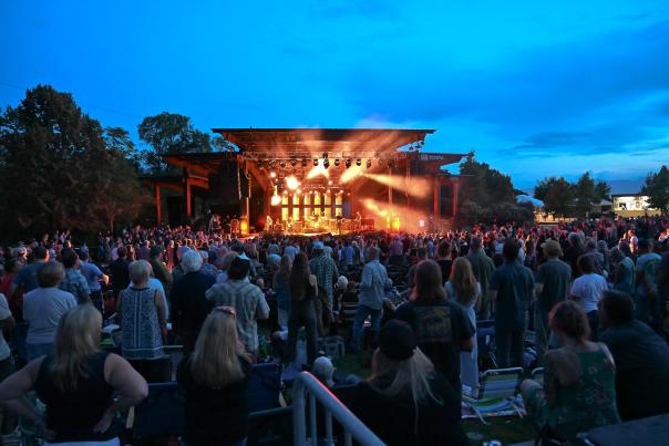 Crowd of people at dusk watching a brightly lit stage with a cool late evening sky