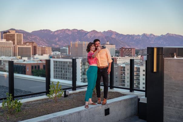 Couple standing and taking a selfie on the roof at Van Ryder with Salt Lake City Skyline and wasatch mountains in the background