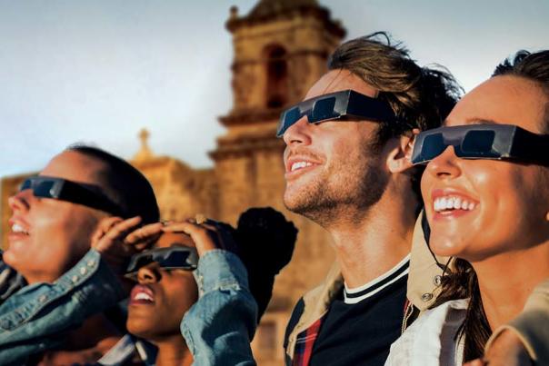 Group of friends in front of San Antonio Missions watching eclipse with protective eyewear