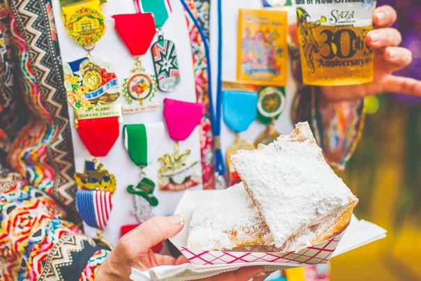 Person holding pastries in powdered sugar wearing Fiesta medals
