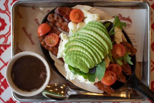 Overhead view of coffee and skillet breakfast topped with avocado.