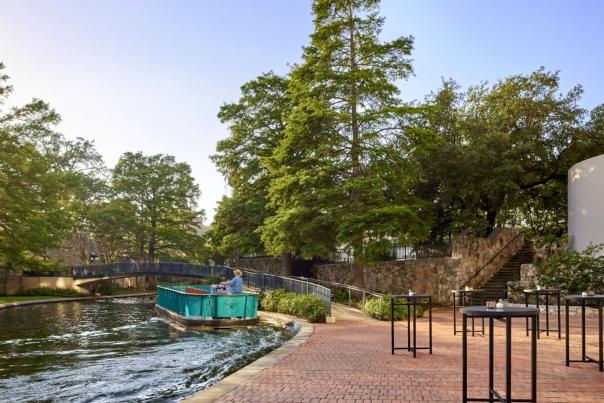 River barge floating along River Walk with large trees in background