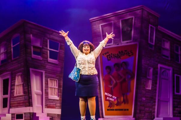 The character Tracy Turnblad from Hairspray standing center stage with her arms raised.
