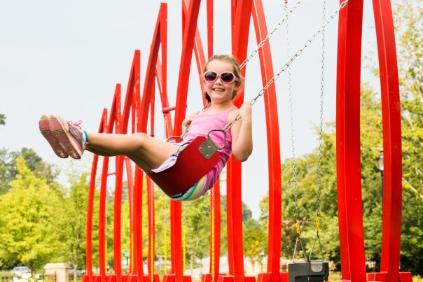 Young girl in a pink outfit swing on big red swings