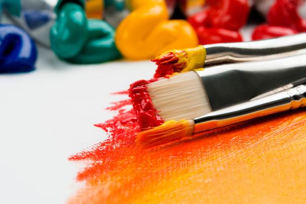 Paint brushes with red and orange paint on a white canvas.
