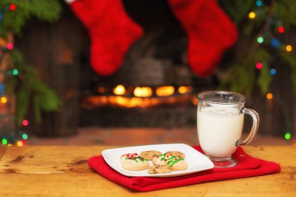 Chocolate Chip and Snowman Shortbread Cookies with a glass of Milk placed on a coffee table. In the background stocks and lights are hung by the fireplace
