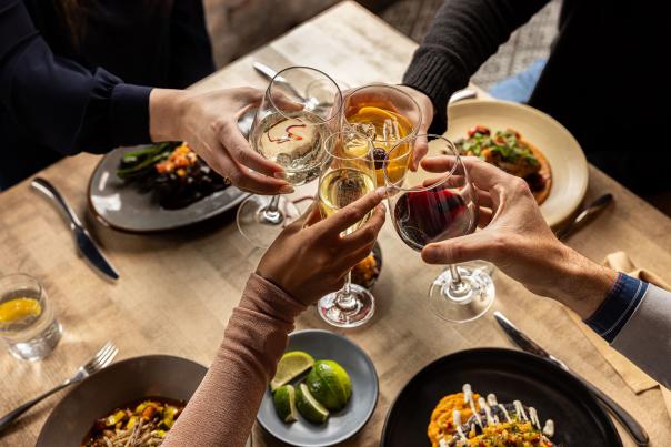 four people cheering their wine glasses over a table of food