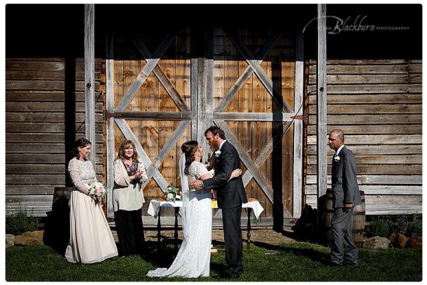 Couple and small wedding party during wedding ceremony in front of barn