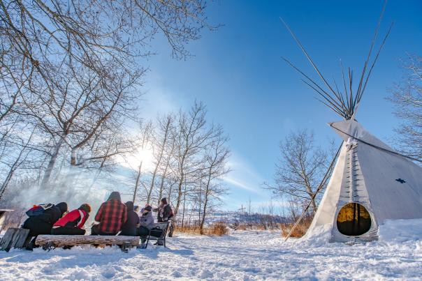 A winter scene with people around the fire and a tipi