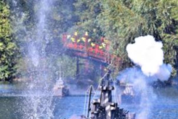A miniature battleship locked in combat on Peasholm Park lake surrounded by smoke and water