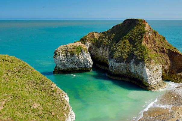 An almost tropical secluded beach, kissed by turquoise waters and flanked by sheer, grass-topped rocky outcrops