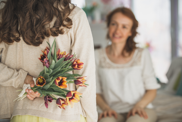 Rear view of a girl holding a bunch of flowers behind her back that she is about to present to the smiling woman facing her