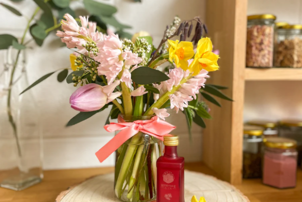 A vase of spring flowers on a wooden table plynth made from tree bark next to a bottle of East Chase Distillers Gin