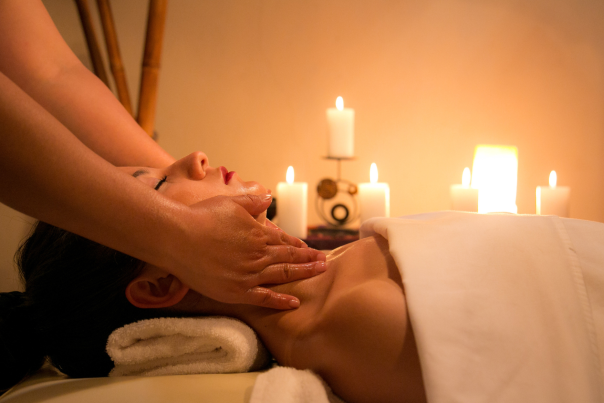A woman lying on a spa treatment bed in a candlelit room with her eyes closed having a massage