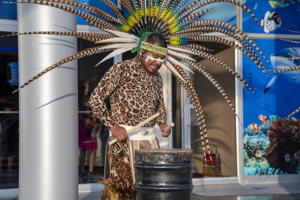 Man with a colorful feather headdress playing the drums on a metal bin