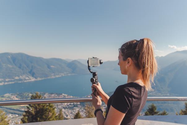 A woman filming with cell phone and gimbal in the mountains over Lake Maggiore