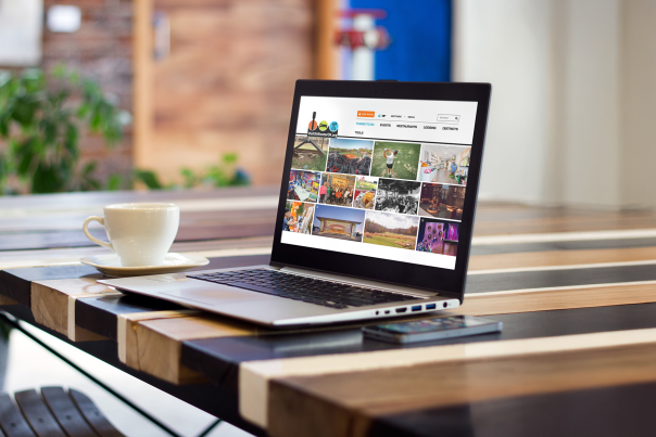 A laptop displaying the Visit Stillwater website sits on a table next to a cup of coffee and a phone.