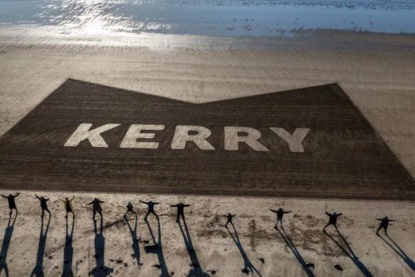 Onlookers on beach facing Discover Kerry logo with arms raised