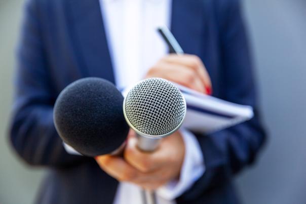 A female journalist takes notes while holding two microphones