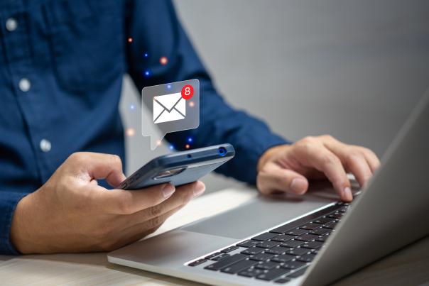 A person takes a break from typing on their laptop to view email notifications on their phone.