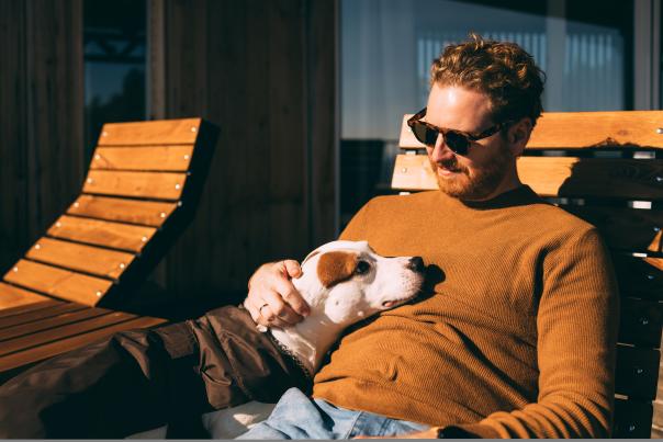 A man lays back on a chair while petting a dog on his lap.