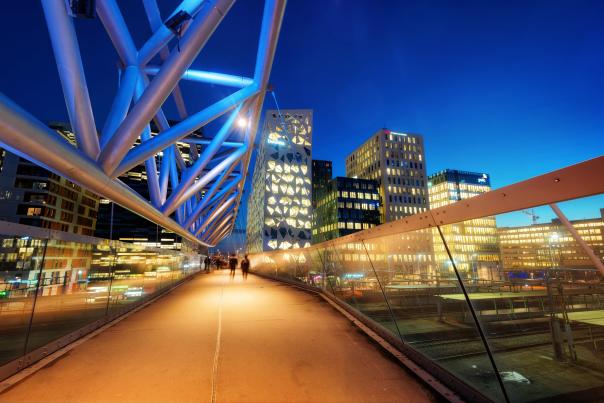People walking across a bridge at nighttime, with a skyline in the background
