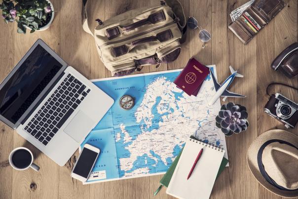 A laptop, cup of coffee, map and compass, among other items, scattered on a table.