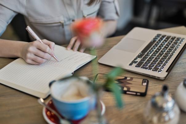 Person Writing On A Notebook Beside Macbook