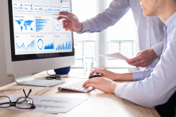Two business men in collared shirts look at a computer screen with website analytics on it